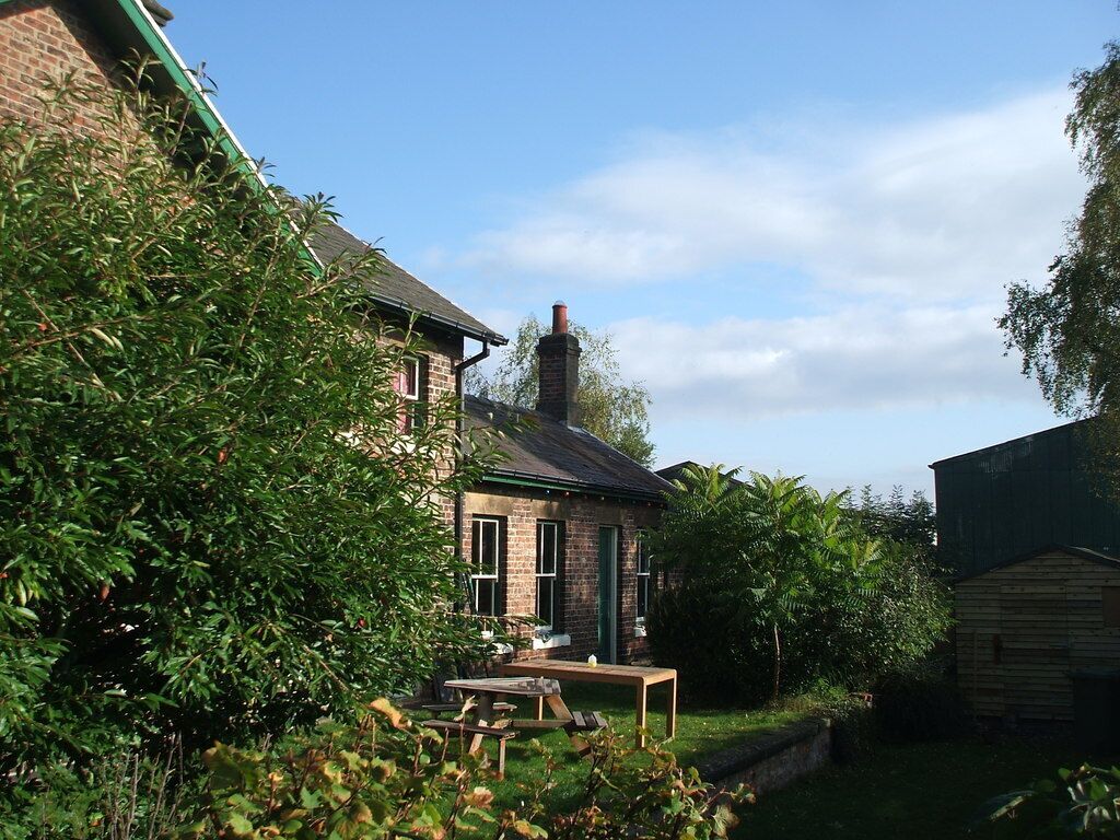 A brick house with a green roof, surrounded by lush greenery and a wooden shed.