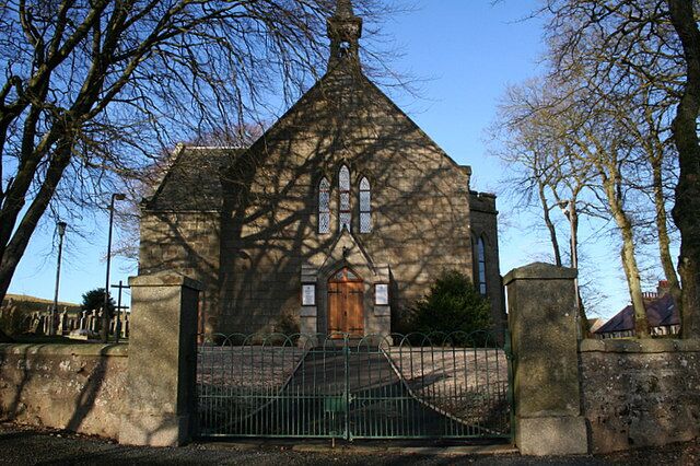 A church with a pointed roof, a wooden door, and a stone fence in front.