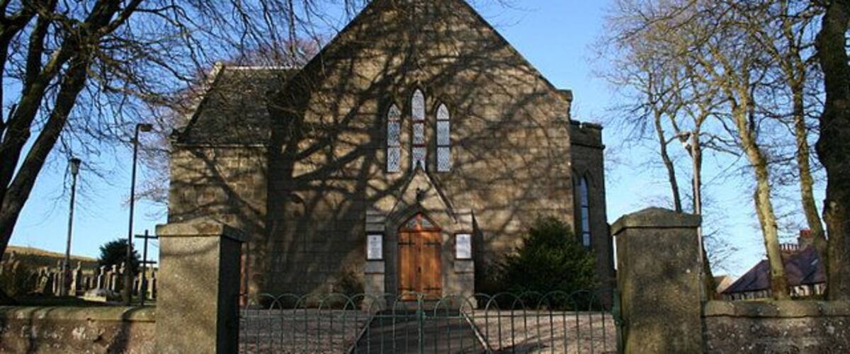 A church with a pointed roof, a wooden door, and a stone fence in front.
