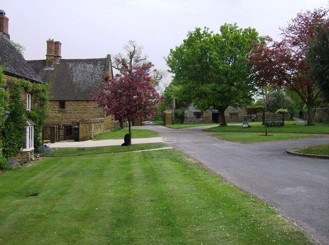 A quiet residential street with stone houses, a well-maintained lawn, and a large tree with pink blossoms.