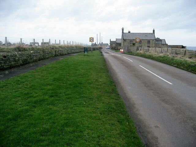 A rural road with a speed limit sign, a stone wall, and a stone building.