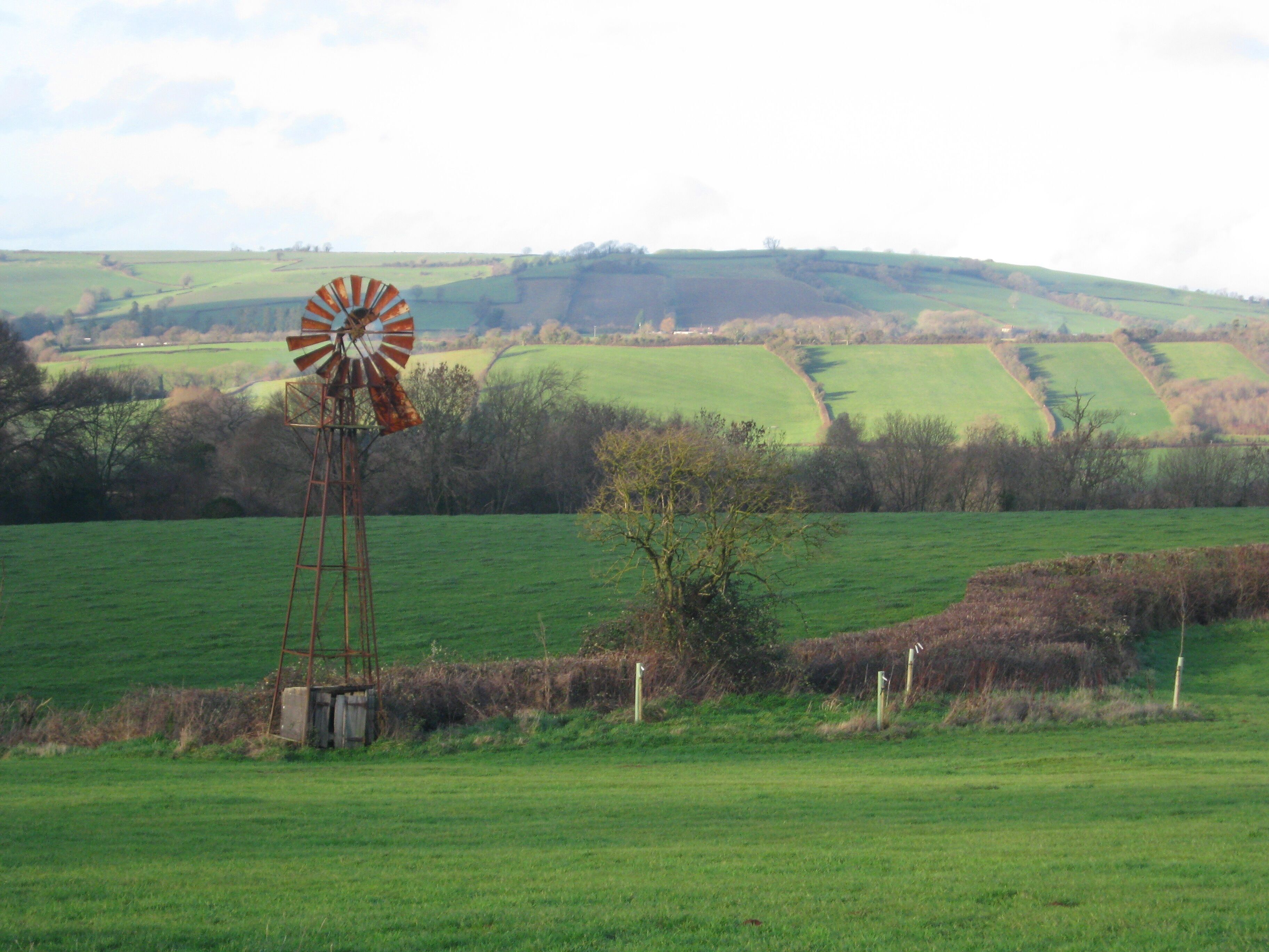 A windmill in a green field with rolling hills in the background.