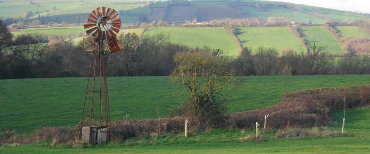 A windmill in a green field with rolling hills in the background.