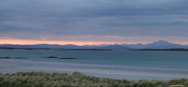 A coastal landscape with mountains in the distance and a calm sea.
