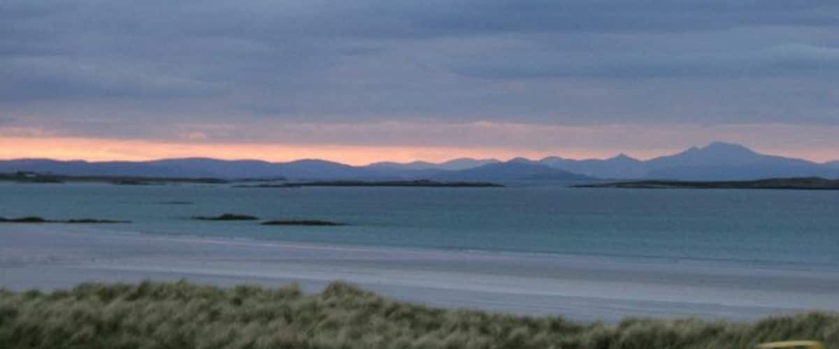 A coastal landscape with mountains in the distance and a calm sea.