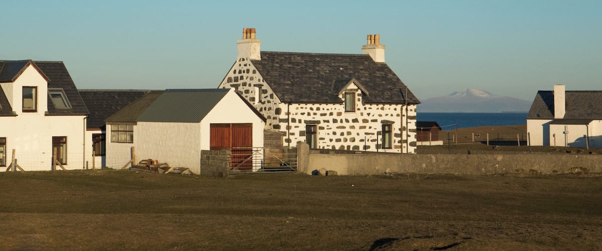 A rural landscape with a stone house, a barn, and a distant mountain.