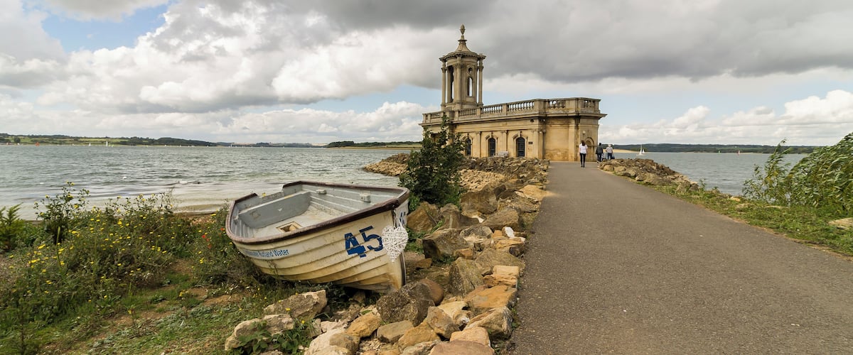 A coastal path with a rowboat, a stone wall, and a historic building with a tower.