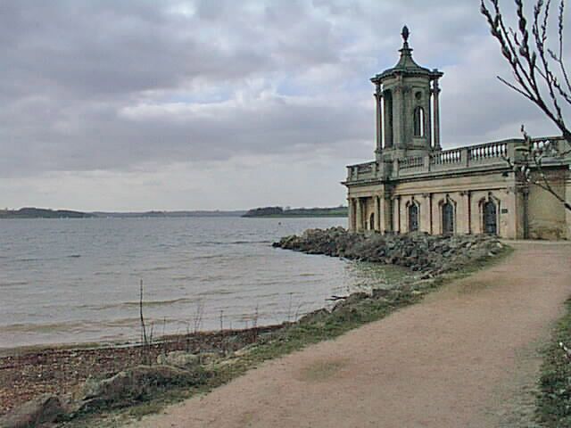 A coastal building with a tower, a path leading to it, and a body of water in the background.
