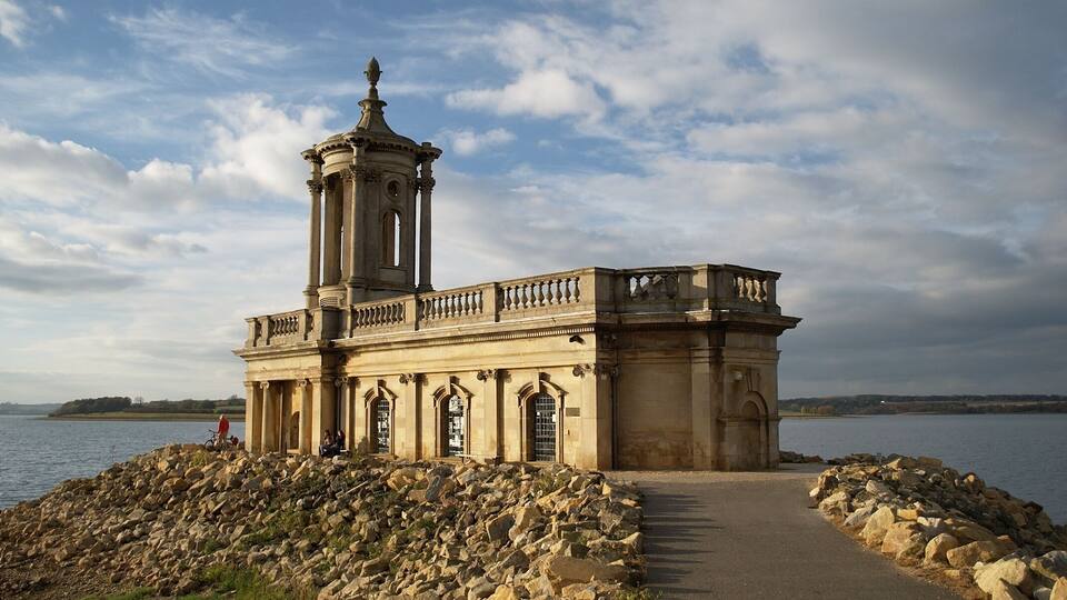 A classical building with columns and a tower by a lake.
