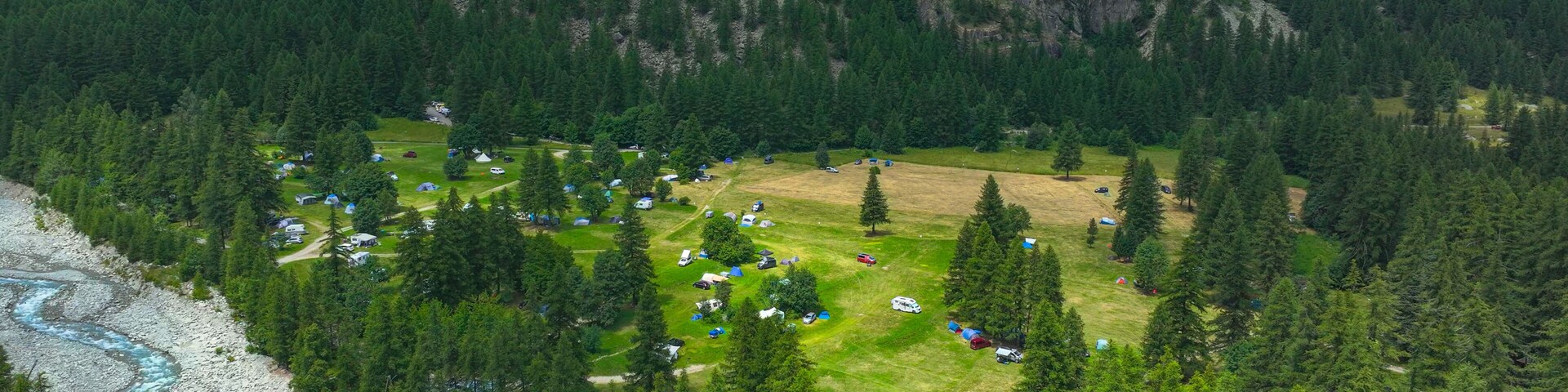 AERIAL: Forest clearing in a mountain valley filled with tents and RVs. Beautiful campsite, surrounded by dense pine trees and high rocky cliffs offers a serene retreat in natural alpine environment.