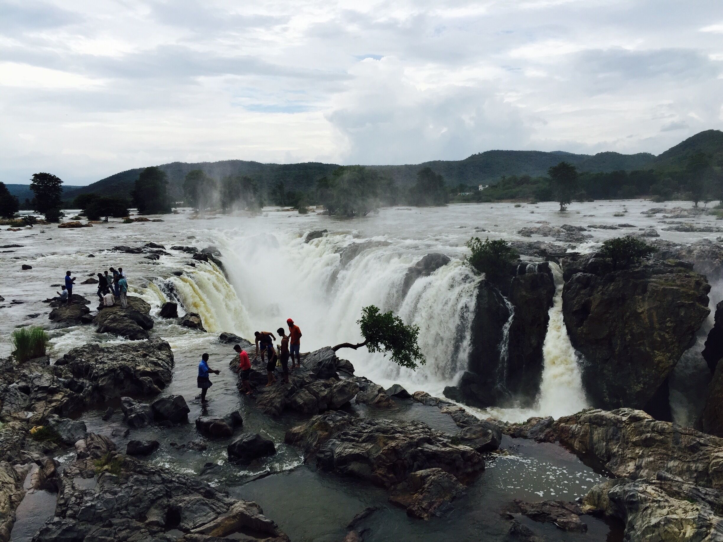 A large waterfall with people standing on rocks in the foreground.