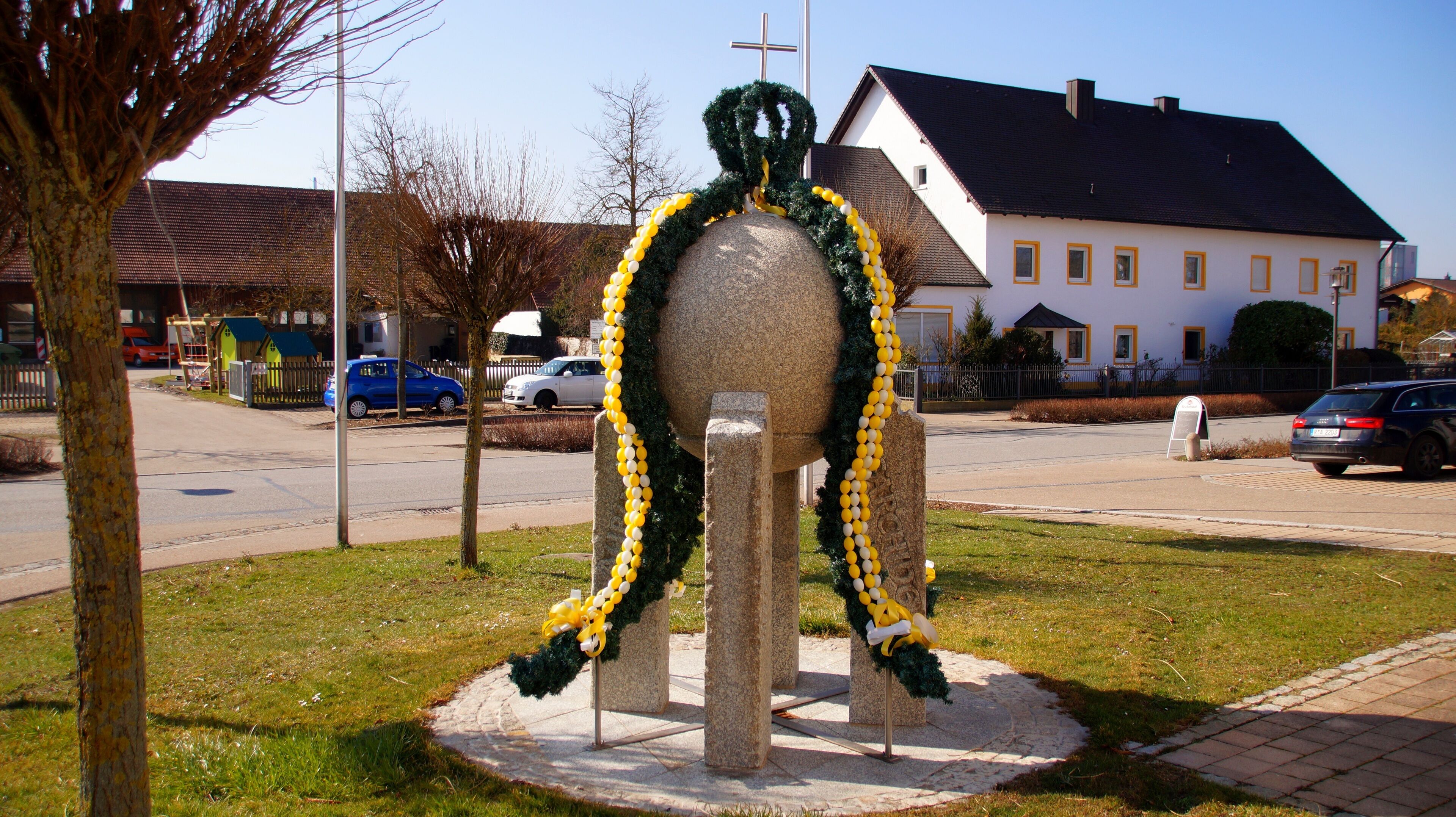 A stone sculpture with yellow and white balloons, a church, and a residential building.