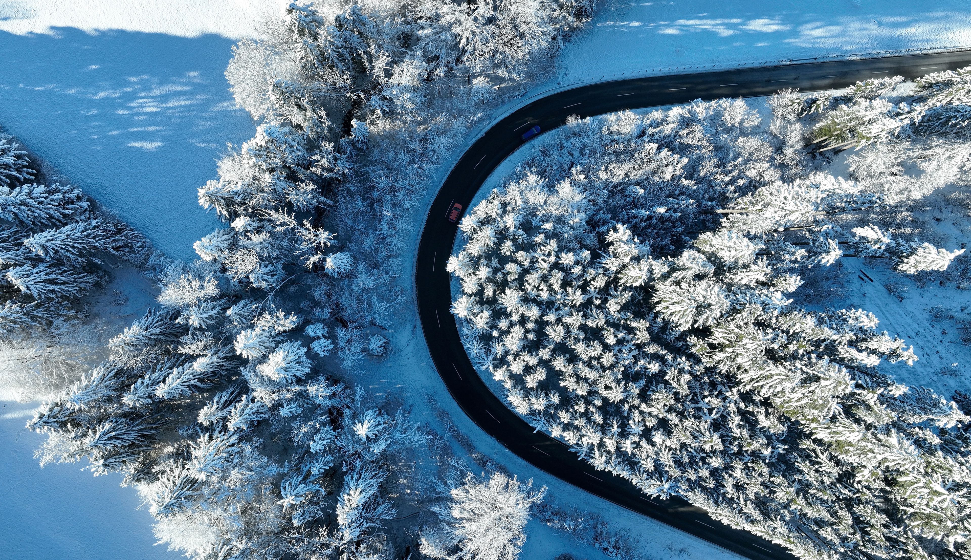 A snow-covered landscape with a winding road and dense trees.