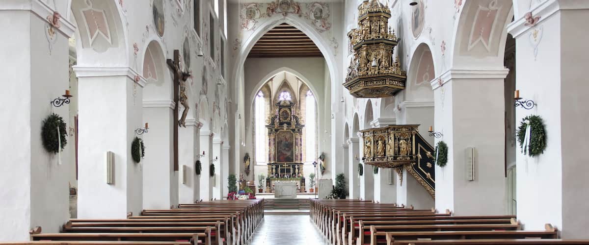 An ornate church interior with wooden pews, arched ceilings, and a central altar.