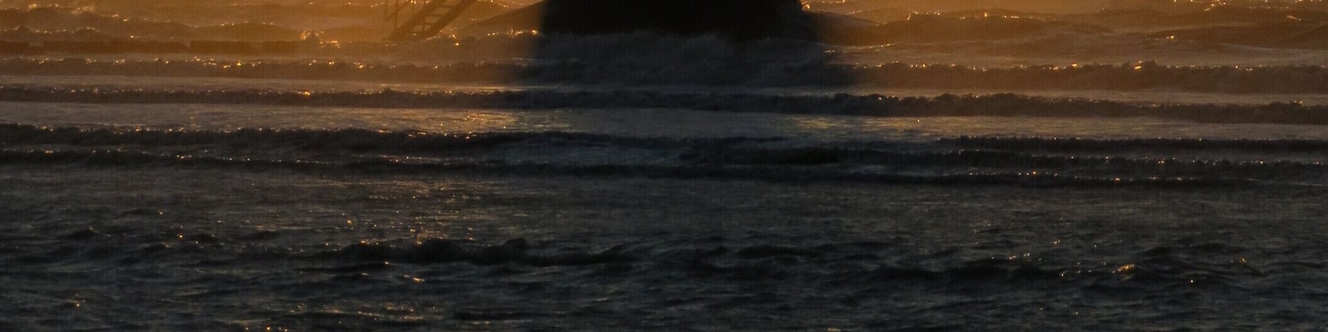 A lighthouse at sunset with the sun setting behind it.