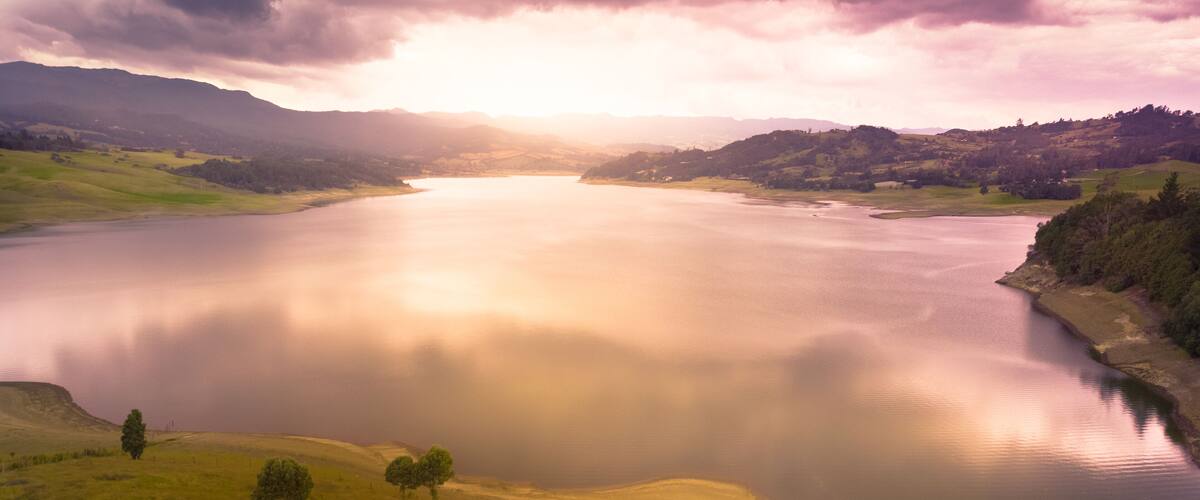 A calm lake surrounded by rolling hills and sparse trees.