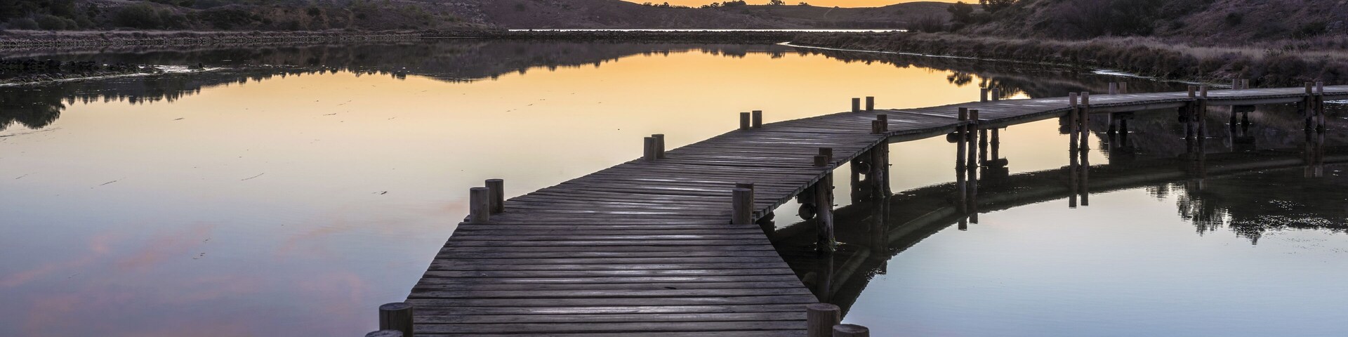 Hills, trees and footbridge reflected in the former salt ponds of Peyriac-de-Mer, Aude, France