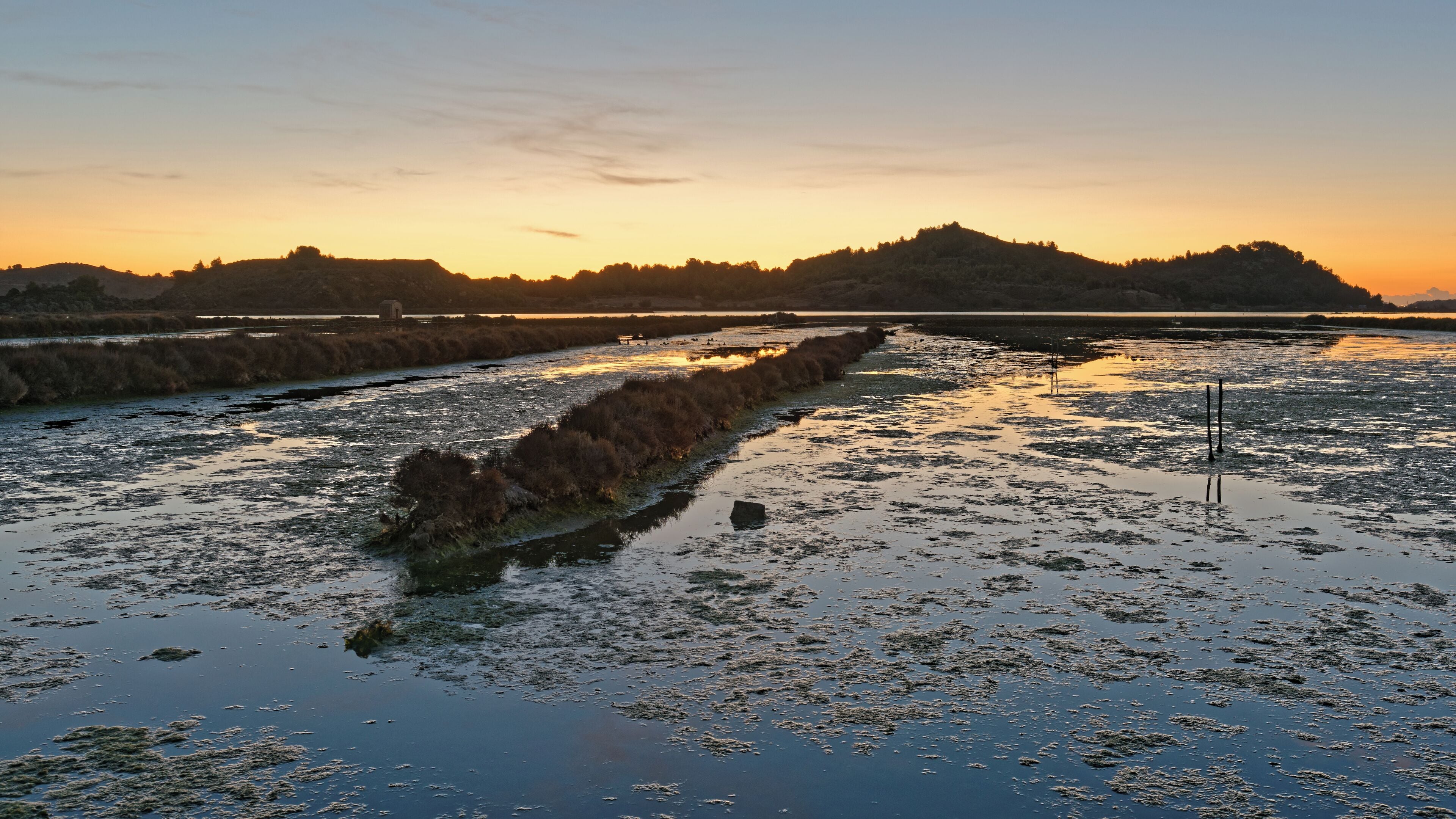 A riverbank at sunset with a distant hill and sparse vegetation.