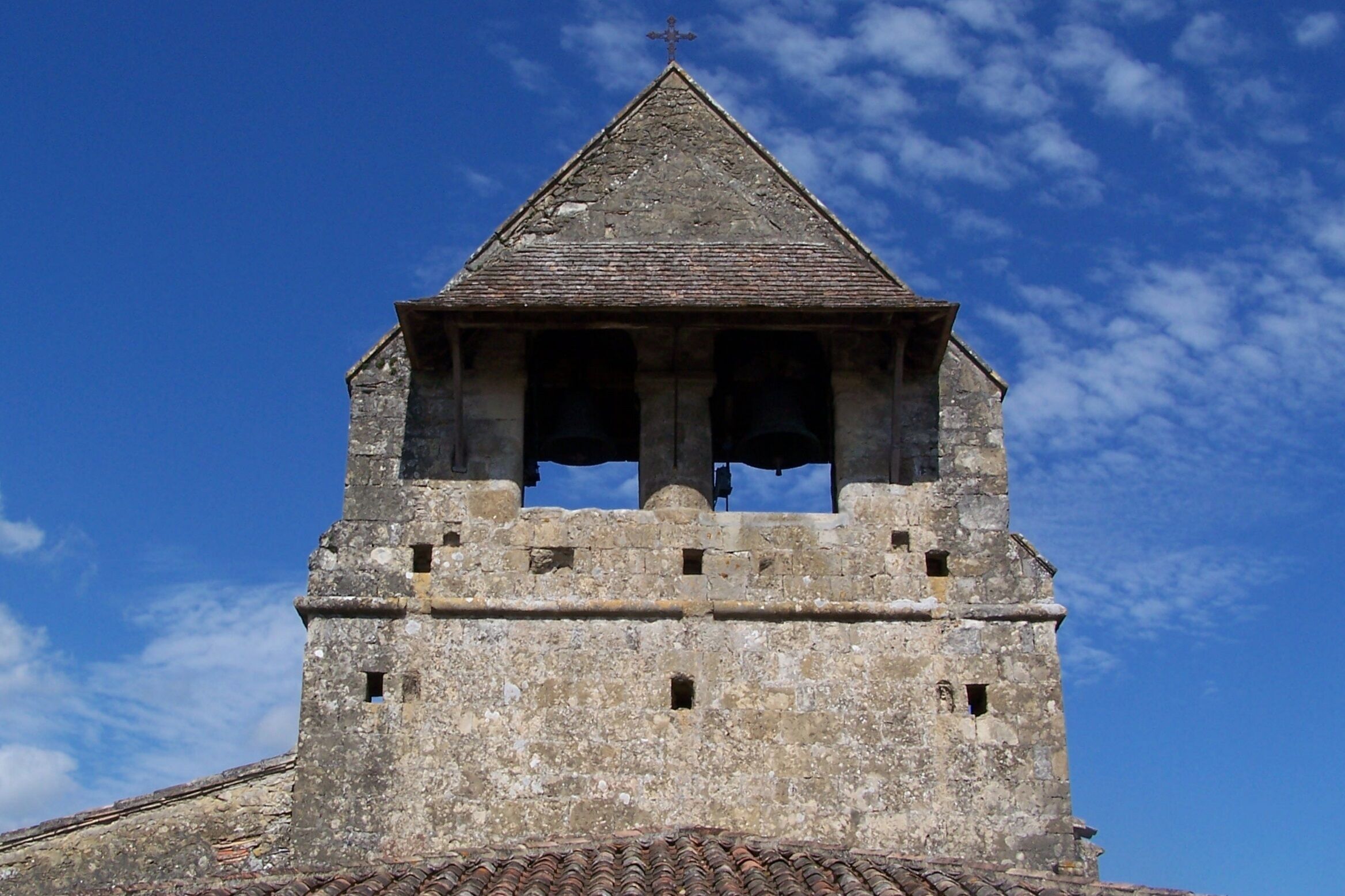 A stone bell tower with a triangular roof and a cross at the top.