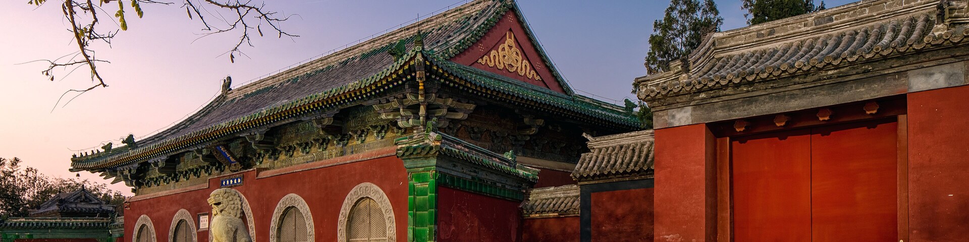 Um edifício tradicional chinês com telhado vermelho, detalhes verdes e uma estátua de leão na frente.