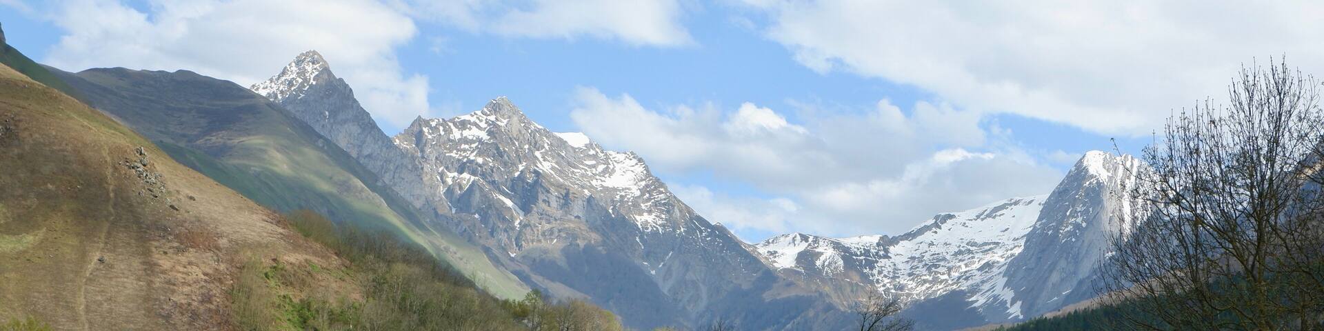 A breathtaking landscape showcases snow-covered peaks towering over lush green fields in Bedous, France