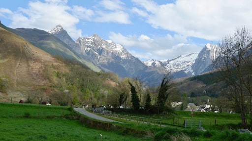 A breathtaking landscape showcases snow-covered peaks towering over lush green fields in Bedous, France