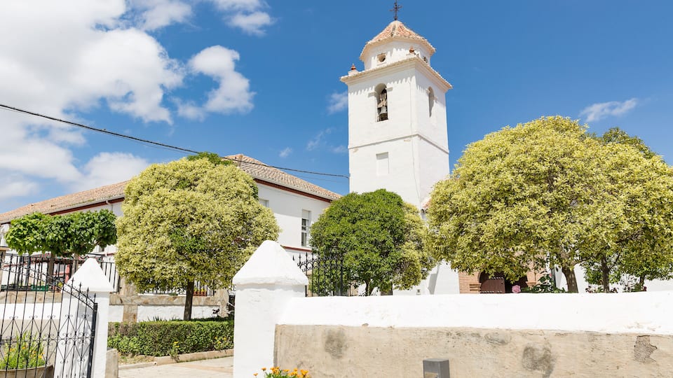 A white church with a bell tower, surrounded by trees and a white wall.