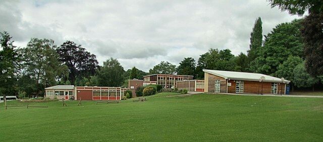 A building complex with a large lawn in front, surrounded by trees.