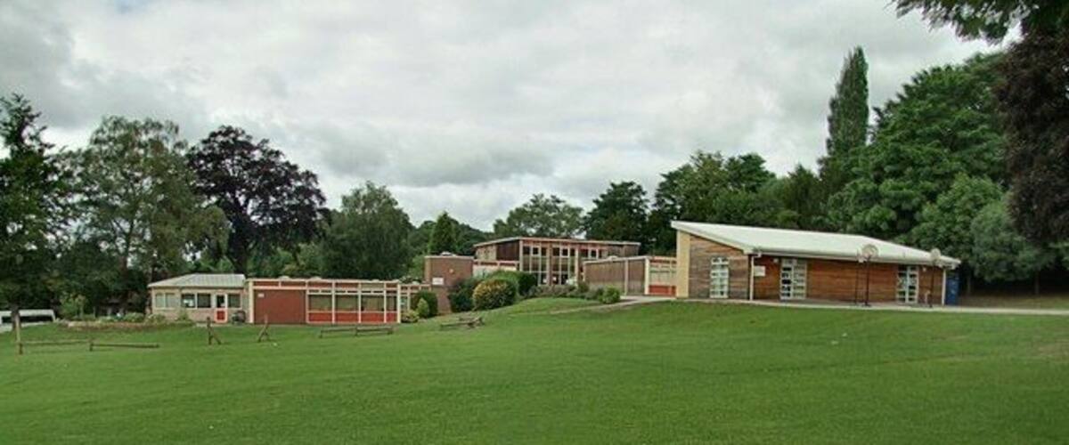 A building complex with a large lawn in front, surrounded by trees.