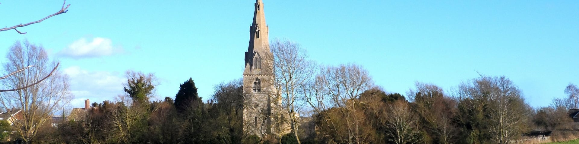A church tower in a green field with trees and houses in the background.