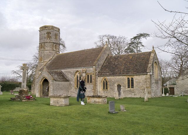A stone church with a bell tower, a grassy cemetery, and a person walking.