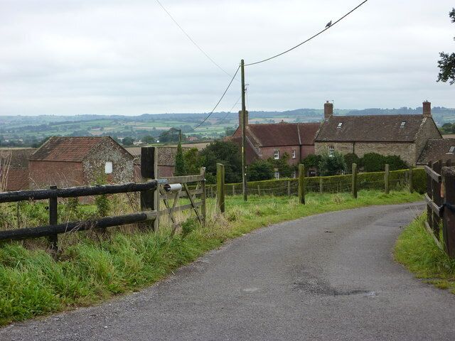 A rural road curving through a countryside with stone houses and a wooden fence.