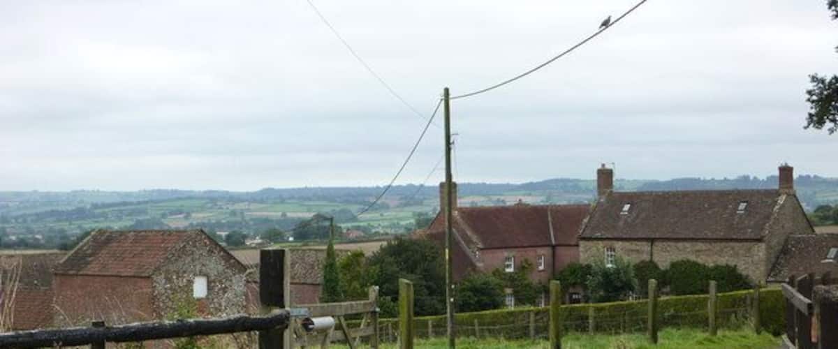 A rural road curving through a countryside with stone houses and a wooden fence.