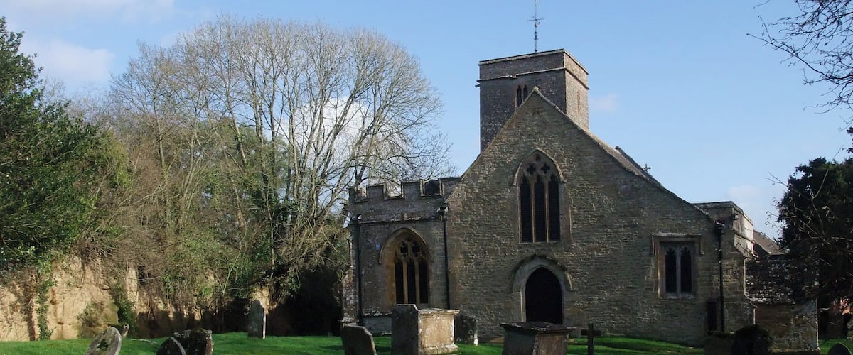 A stone church with a bell tower, surrounded by a cemetery with gravestones.