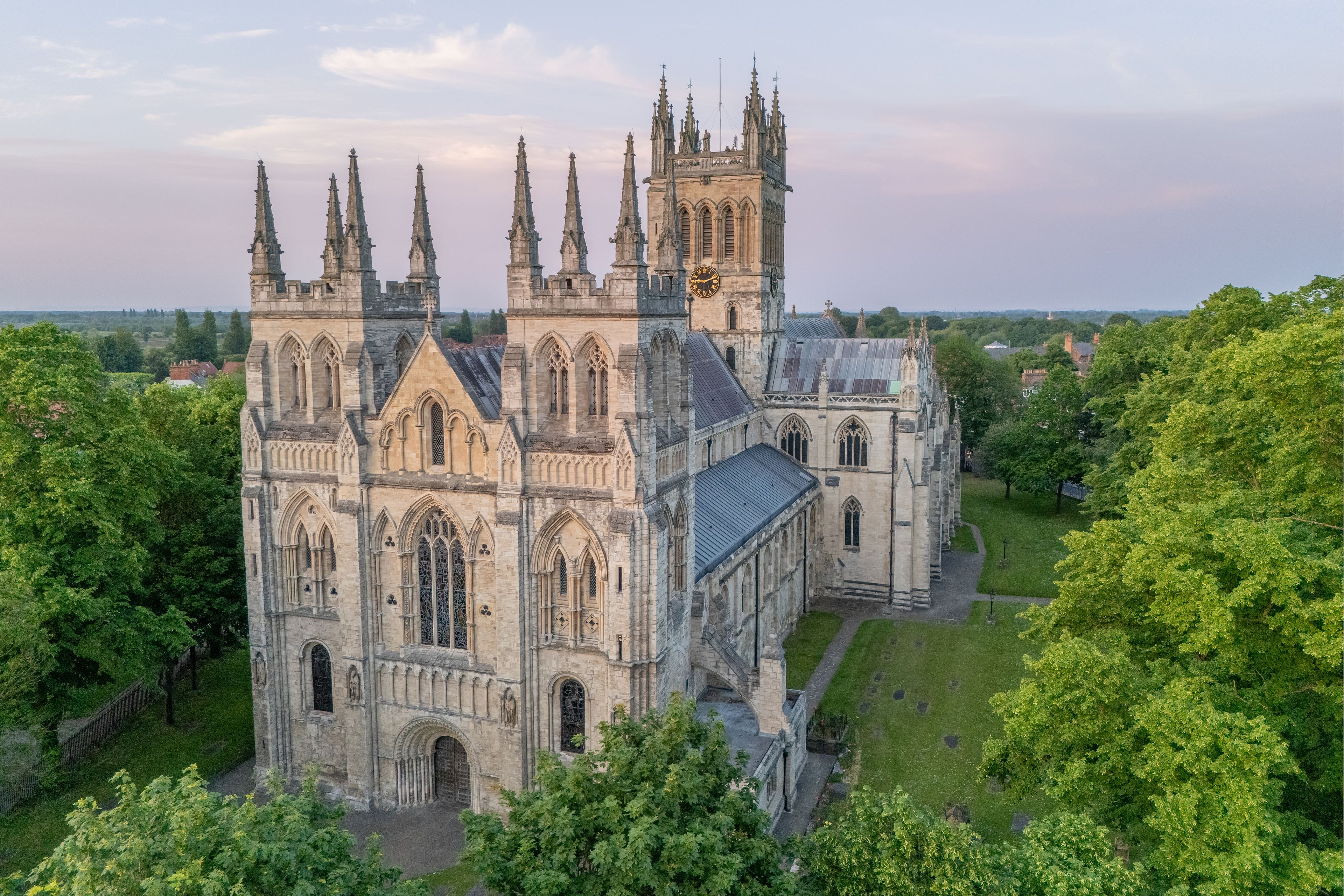 A large Gothic-style cathedral with multiple spires and a clock tower, surrounded by lush green trees.