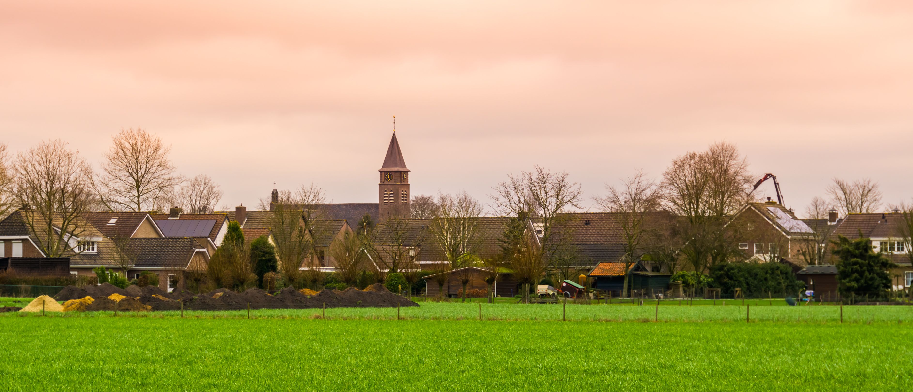 Un paysage rural avec un clocher d’église, des maisons et un champ verdoyant.