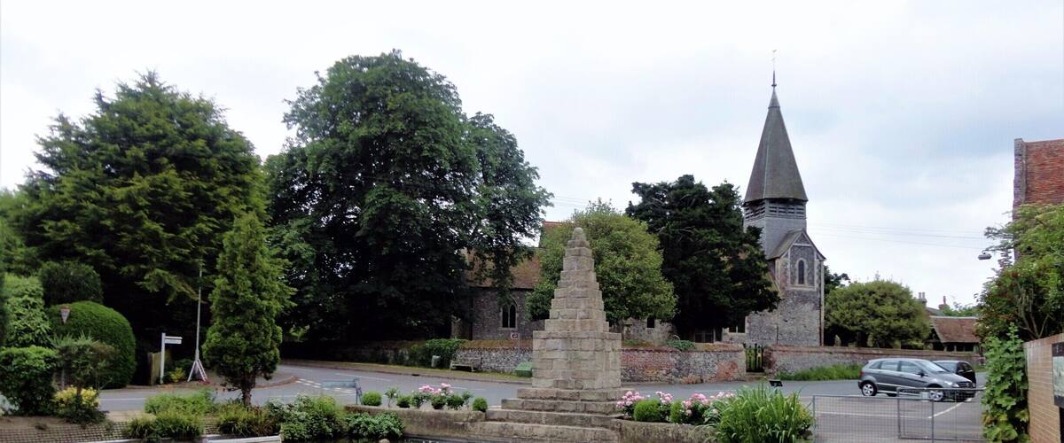 A pond with ducks, a stone monument, and a church with a steeple.