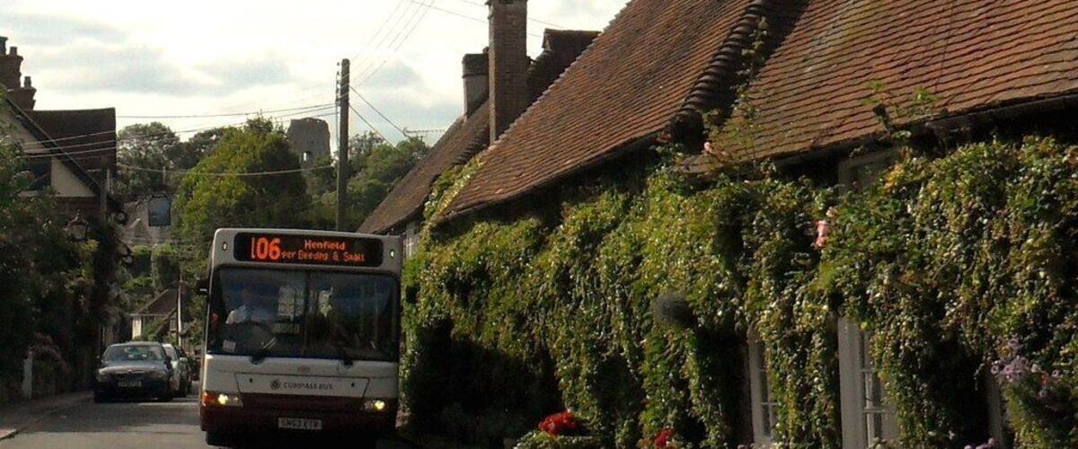 A bus on a rural road with houses covered in ivy and red flowers.