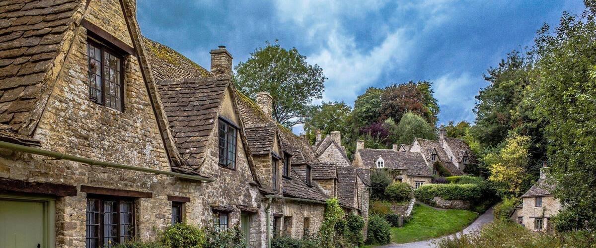 A narrow stone road winding through a village with traditional stone houses and lush greenery.