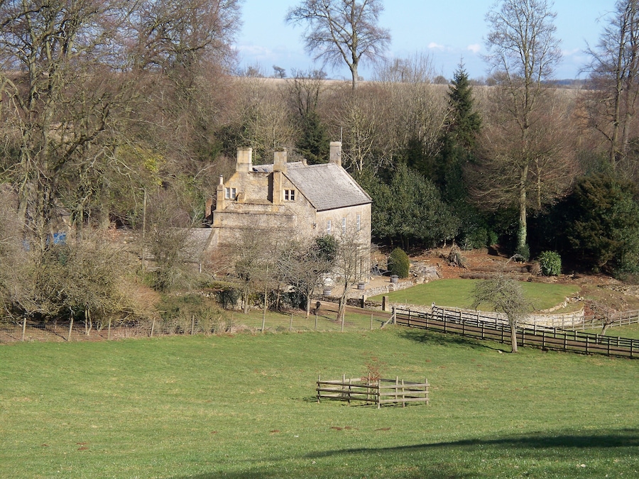 A stone house surrounded by a fenced field and trees.