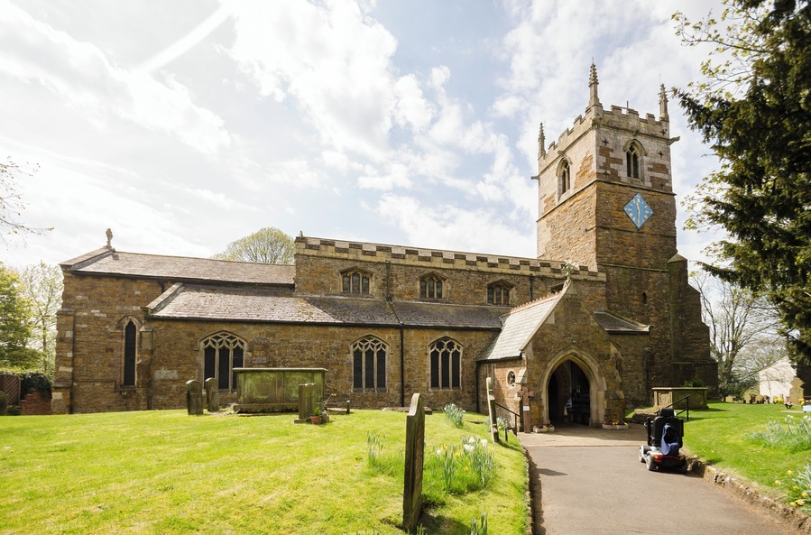 The church dates from the 11th century onwards and was rebuilt and restored in the 19th century. Certainly there was a church here in Saxon times and the lower part of the tower is probably Saxon, from around 1050. There is a west tower, nave with clerestory and north and south aisles, north porch, vestry and chancel. The tower is built in ironstone and dates from the mid-12th century. It is thought that the lower stage the tower could have been a Norman porch to the old church. The second stage is Early English and the top stage is Perpendicular. The tower has an embattled parapet with pinnacles and gargoyles. The tower arch has zigzag decoration. There are eight bells. The nave has four-bay arcades with octagonal piers and four clerestory windows either side. The chancel arch is from the 13th century. It is thought that the church may have been intended as being a cruciform shape with a crossing, or it may indeed have once been like this. The chancel was largely rebuilt in 1848 and restored in 1873. The reredos is from that date. There are several effigies of Knights set into arched tombs in the wall. There is a triple lancet east window, and stained glass from a variety of makers. The organ is by Cousans, and was installed in 1885. The rood beam is by Wilfrid Bond, erected in 1929.