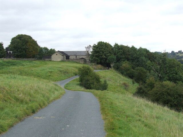 Un camino rural serpentea por un paisaje cubierto de hierba, con un edificio de piedra a lo lejos.