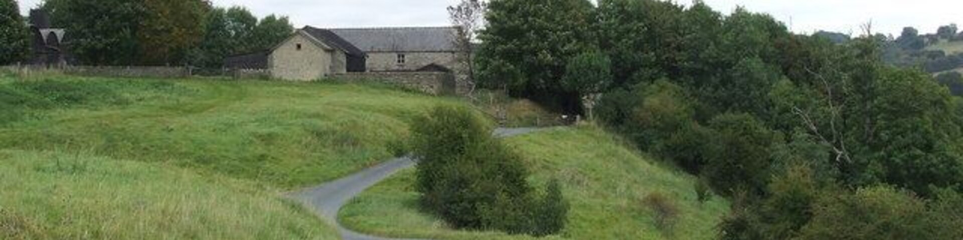 Un camino rural serpentea por un paisaje cubierto de hierba, con un edificio de piedra a lo lejos.