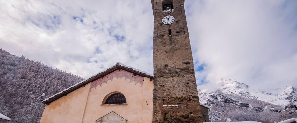 A church with a tall bell tower and snow-covered mountains in the background.