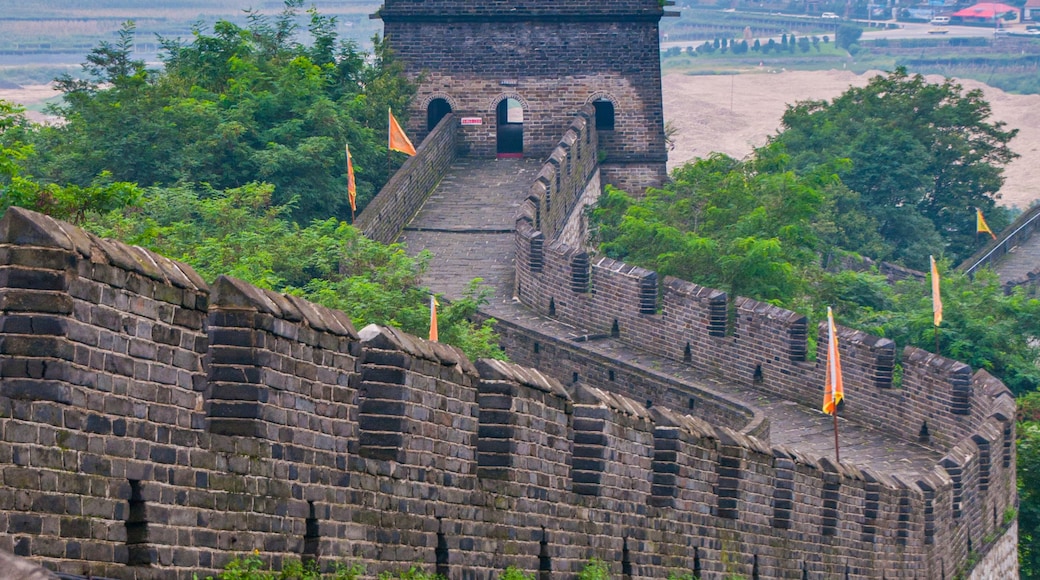 The Great Wall of China with watchtowers and flags, surrounded by lush greenery and distant mountains.