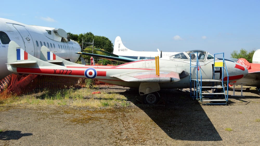 Vintage military aircraft parked outdoors, including a white plane with red and blue markings and a smaller red and white plane with a ladder.
