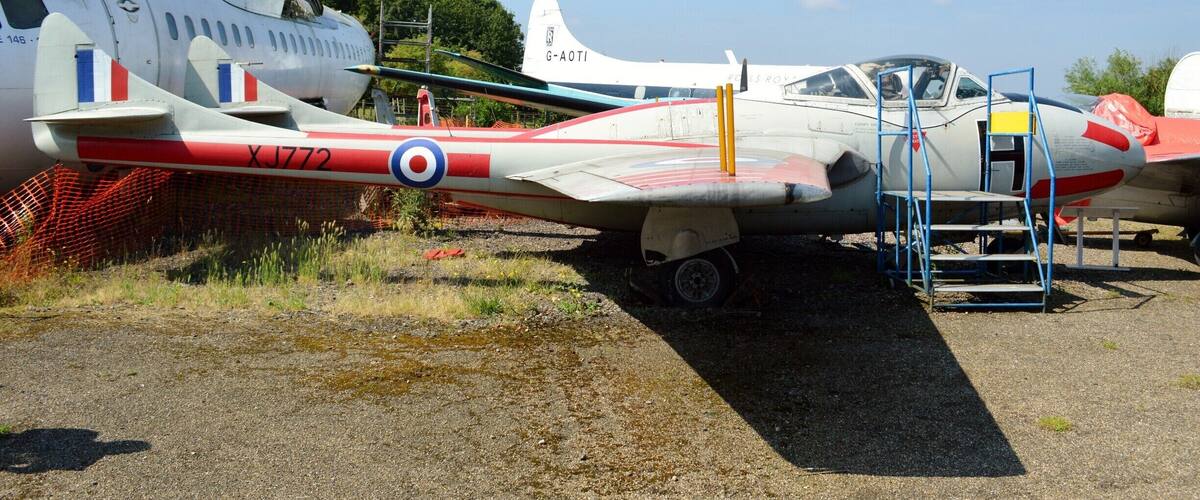 Vintage military aircraft parked outdoors, including a white plane with red and blue markings and a smaller red and white plane with a ladder.