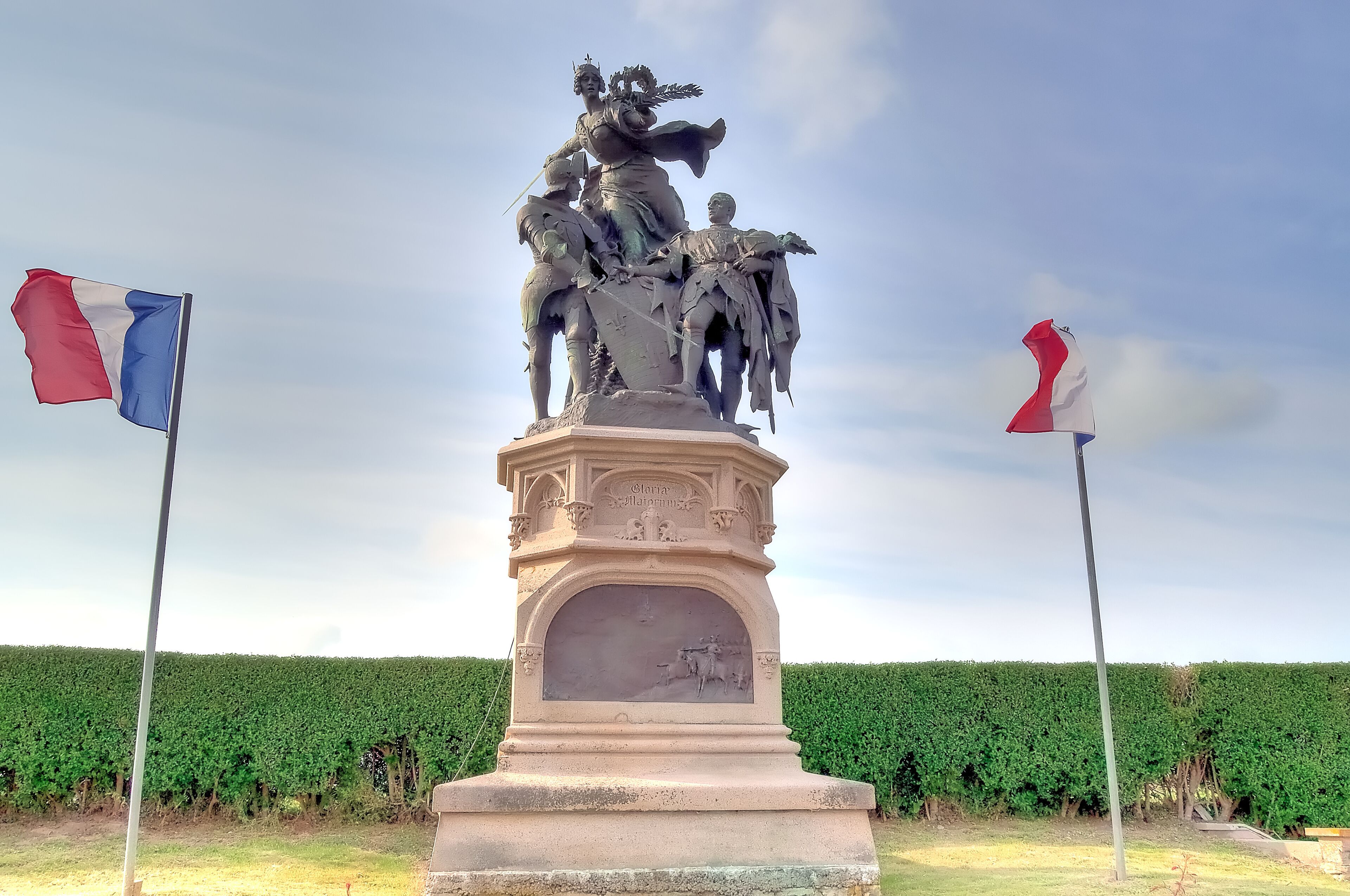 A statue with two flags, set against a hedge backdrop.