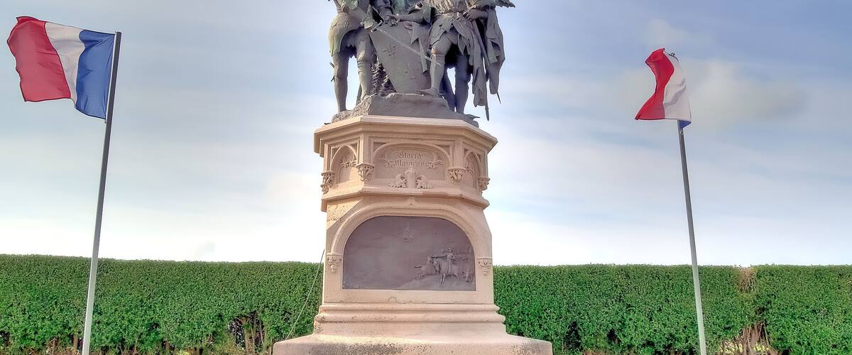 A statue with two flags, set against a hedge backdrop.