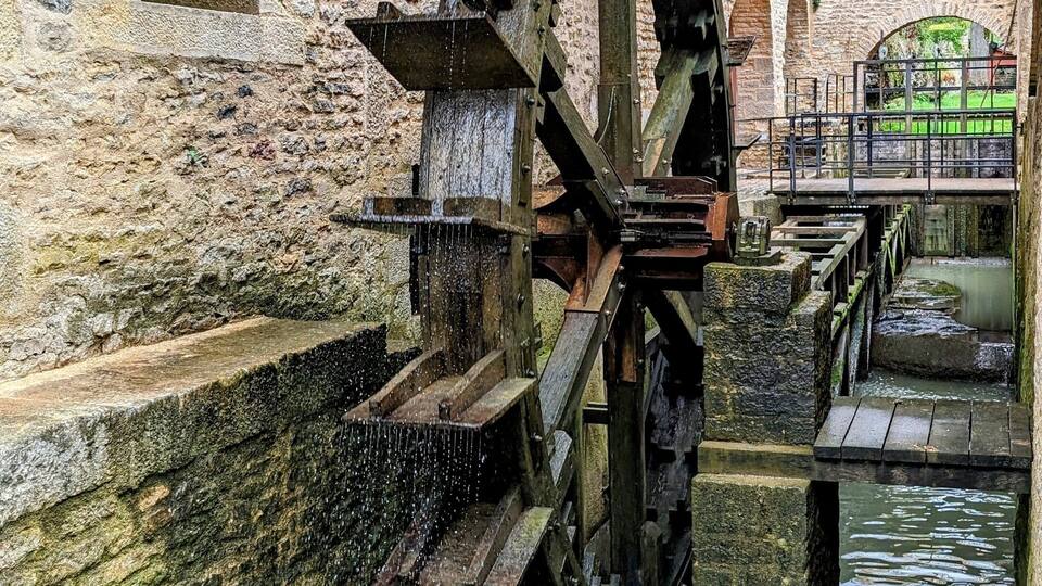 A large water wheel in a stone building with water flowing through it.